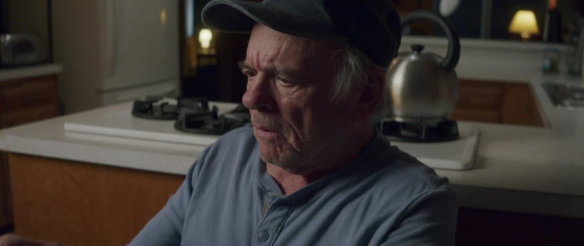 Elderly man sitting laughing in a room of his house at night