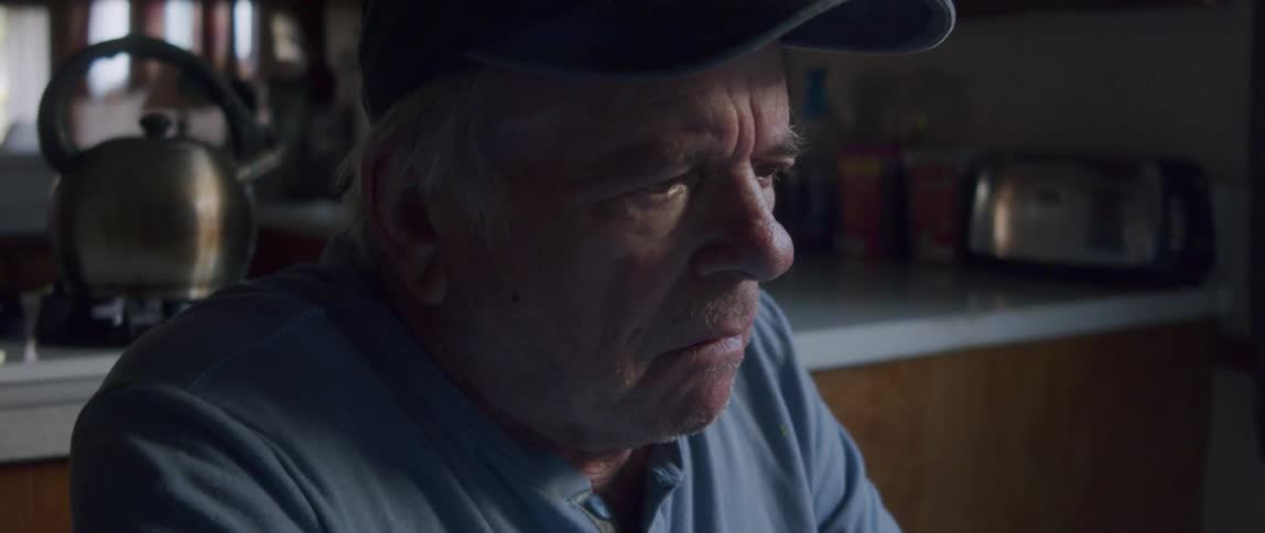 An elderly man sits in the kitchen looking very confused