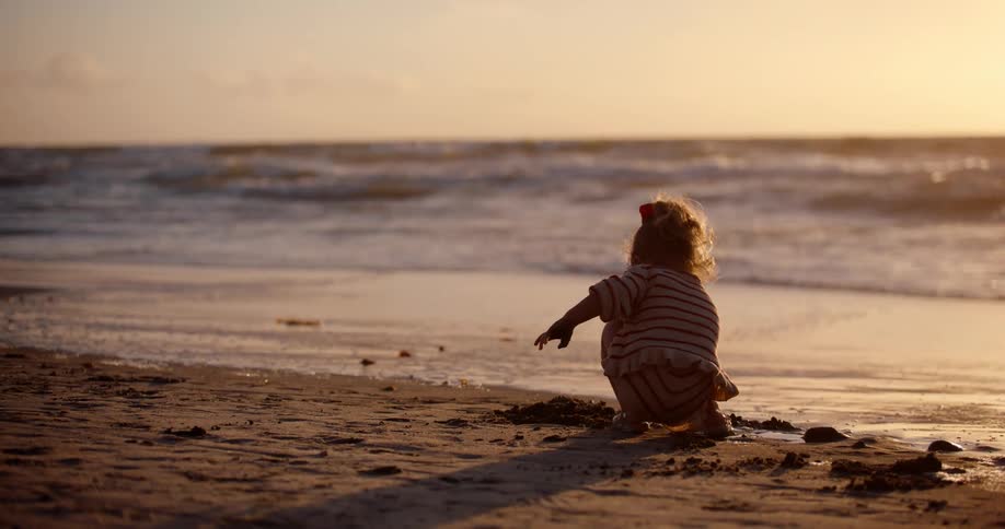 Little girl playing in the sand on the beach with the sunset on the horizon
