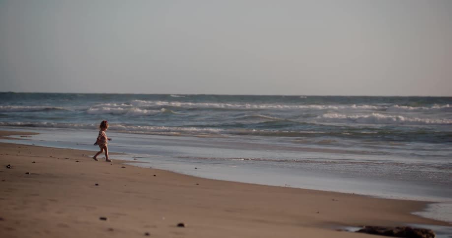 Little girl walking on the sand towards the sea at the beach