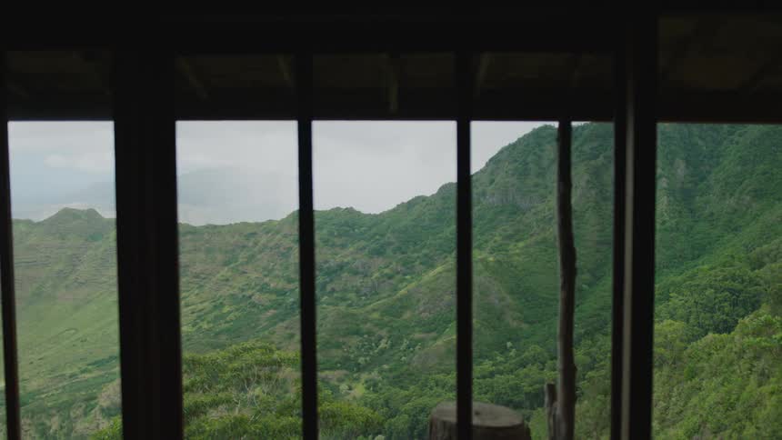 Man in white clothing walking back and forth next to a large window overlooking mountains