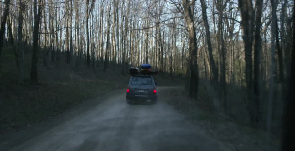 A car with gear strapped on top is driving down a mountain road
