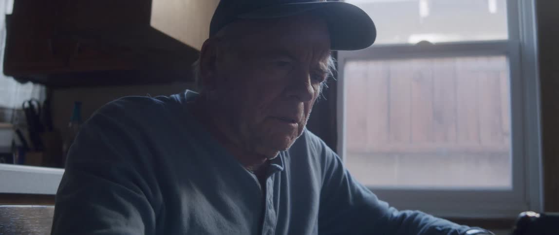 Elderly man sitting at a table interacting with a tablet and looking scared