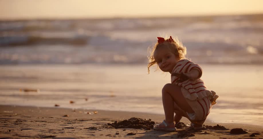 A young blonde girl plays in the sand on the beach at sunset