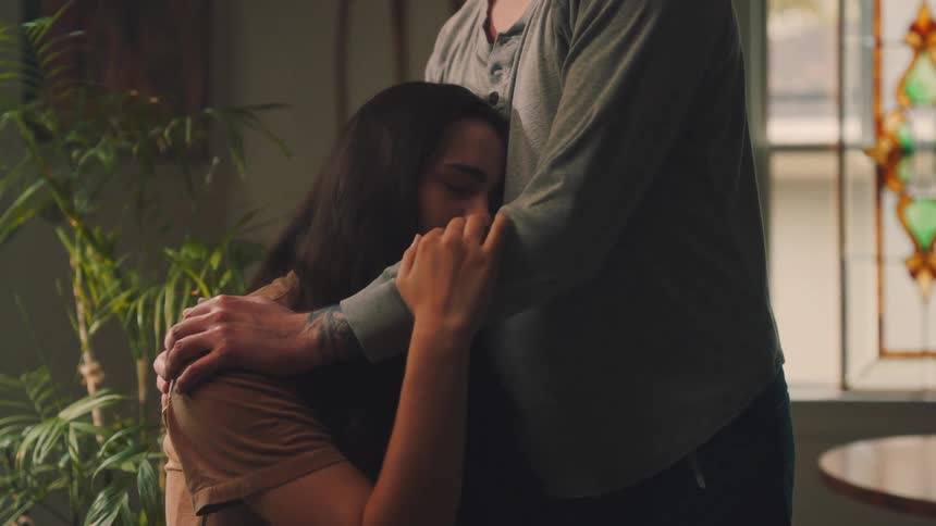 Seated woman being hugged by a person standing