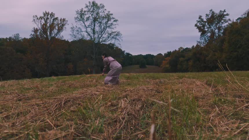A woman in a dress dances in a field of dry grass