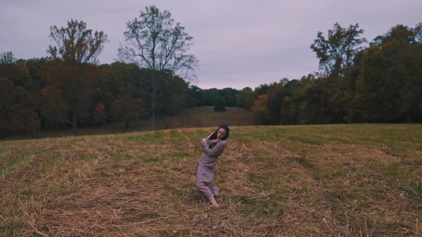 Woman in purple dress performing dancing in a field surrounded by trees