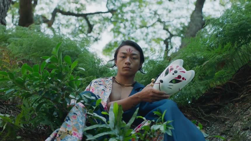 Model with an asian look sitting in a bush revealing her face by removing a mask