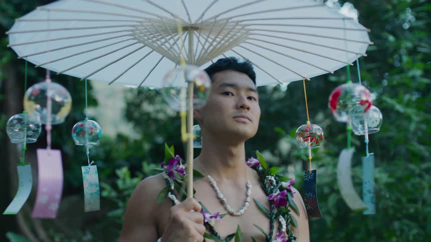 Shirtless man with necklaces posing in a natural environment with an oriental umbrella