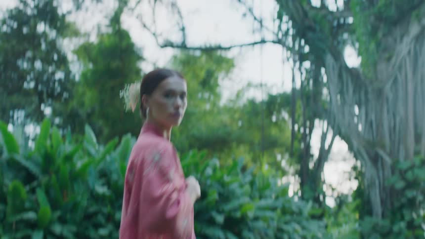 Woman model in a pink kimono standing on the grass in a green environment