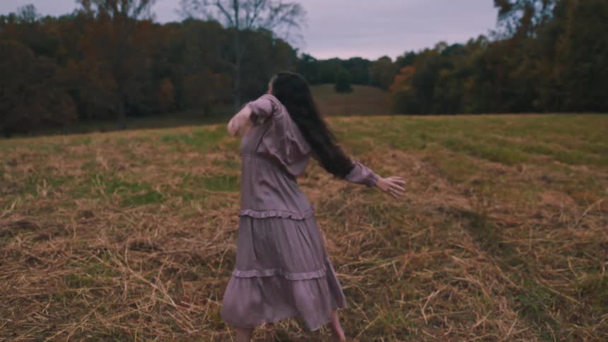 A young woman dances in a grassland on a cloudy autumn day