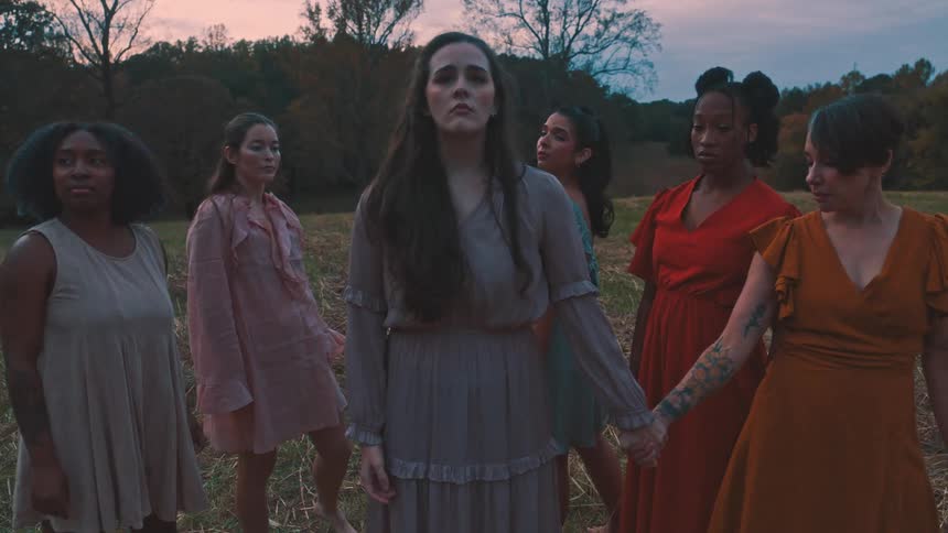 Group of women all wearing different colored dresses in a field performing