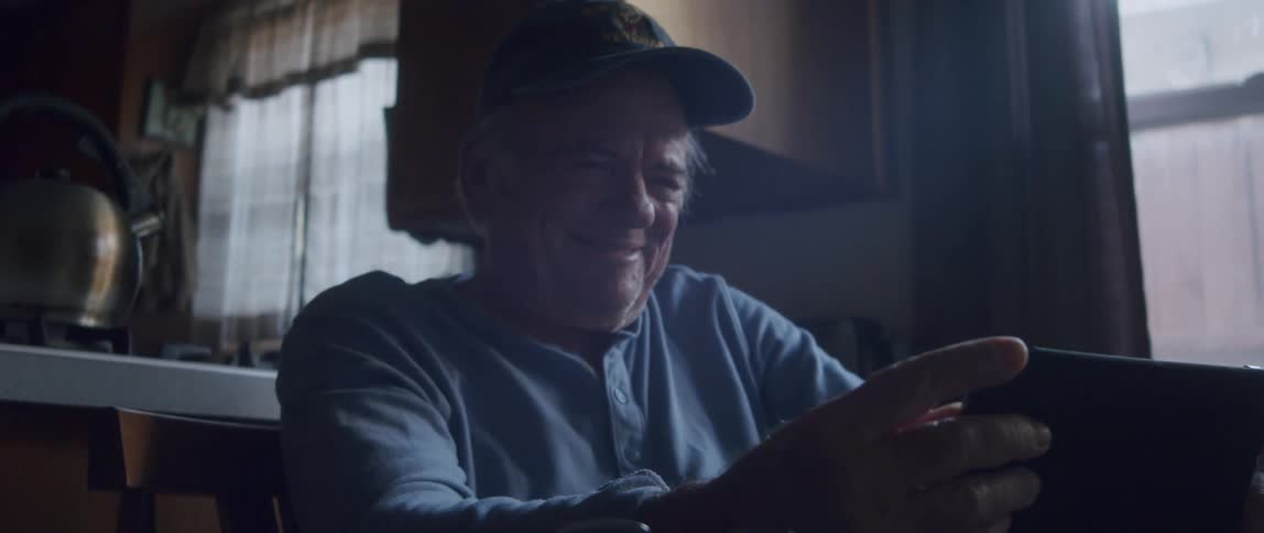 Elderly man holding a tablet sitting at the table and laughing