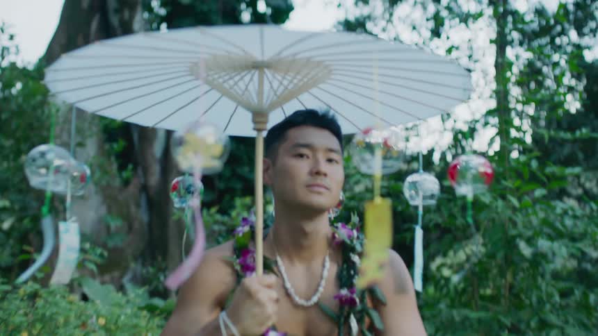 A muscular man in the forest with a flower wreath and a paper umbrella with glass wind chimes
