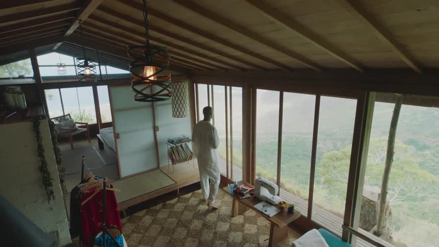 Man drinking from a mug while standing in a house on a hill overlooking a forest