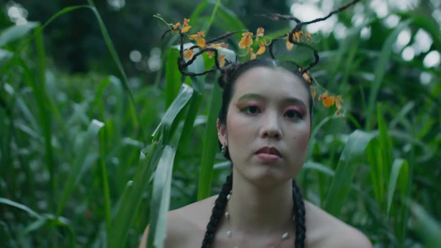 A woman with a floral crown sits in a field of tall grass