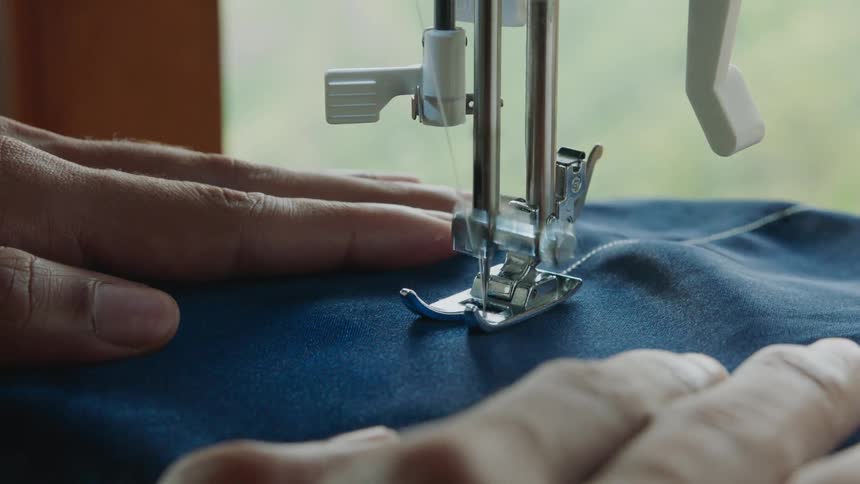Hand shaping blue fabric on a sewing machine