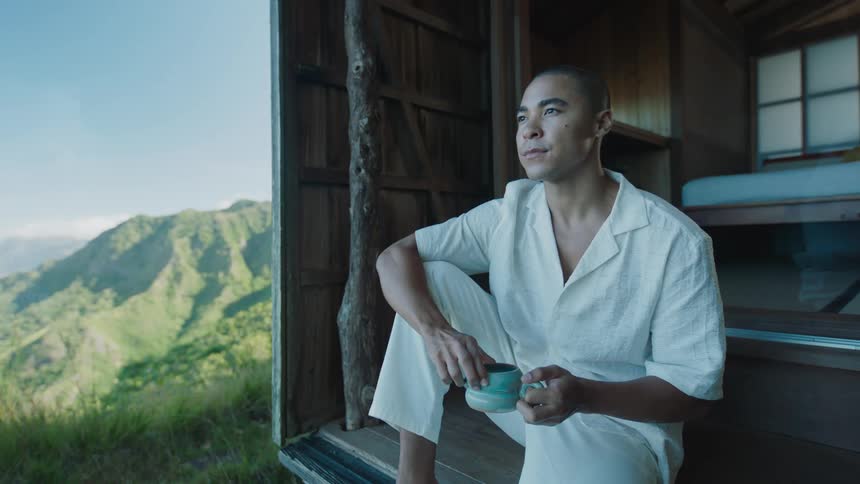 Monk sitting drinking from a mug with mountains in the background