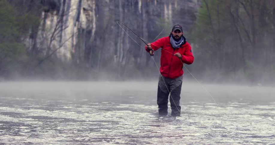 A man standing in water holding a fishing pole and throwing the line