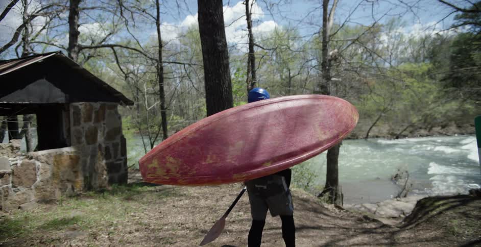 A person carries his kayak and oar to the river