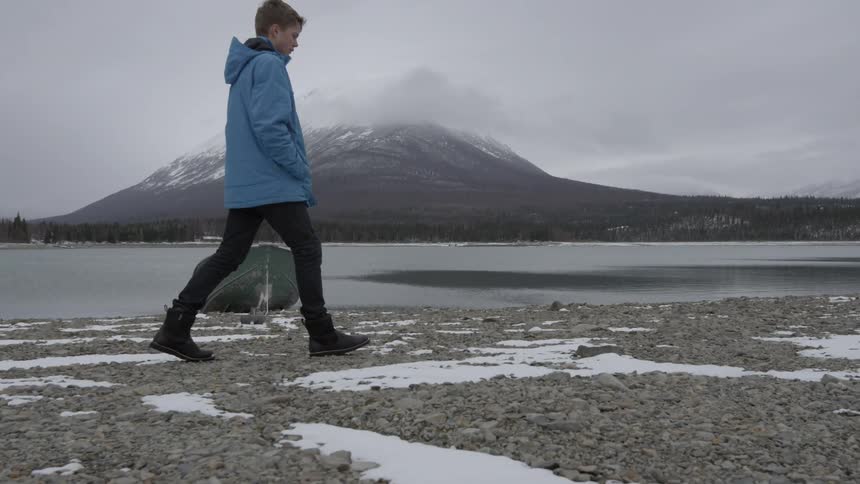 A boy is walking on a shore on a cold day