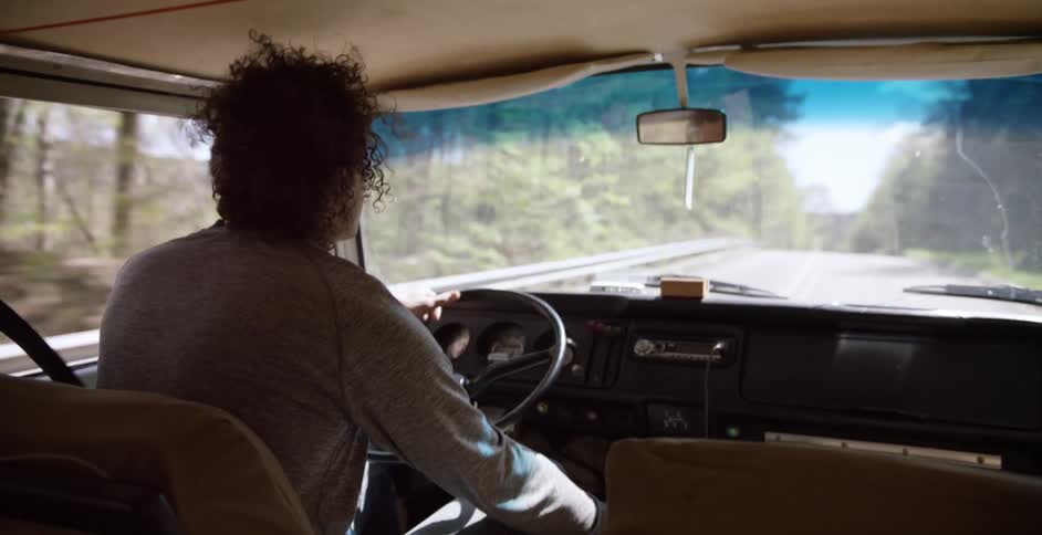 A person with curly hair is driving down a road in the mountains