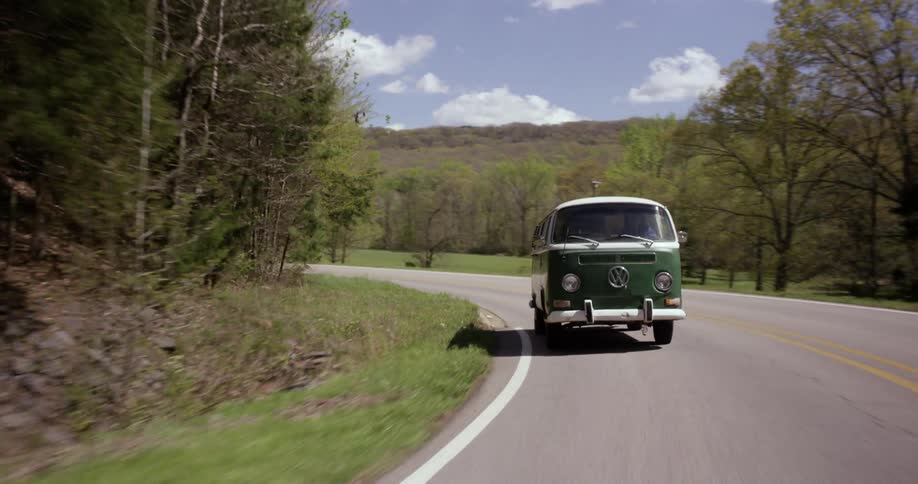 A volkswagen van drives on a rural road