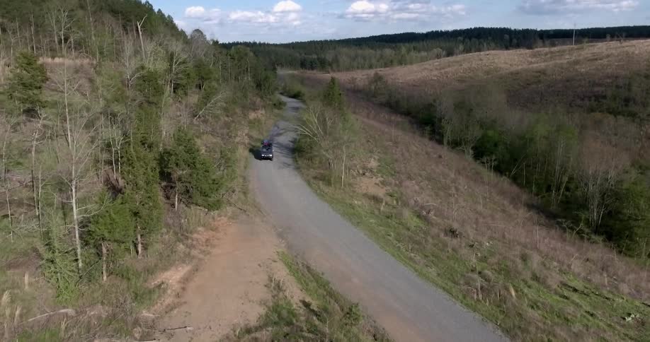 A car driving through the woods is filmed from the air