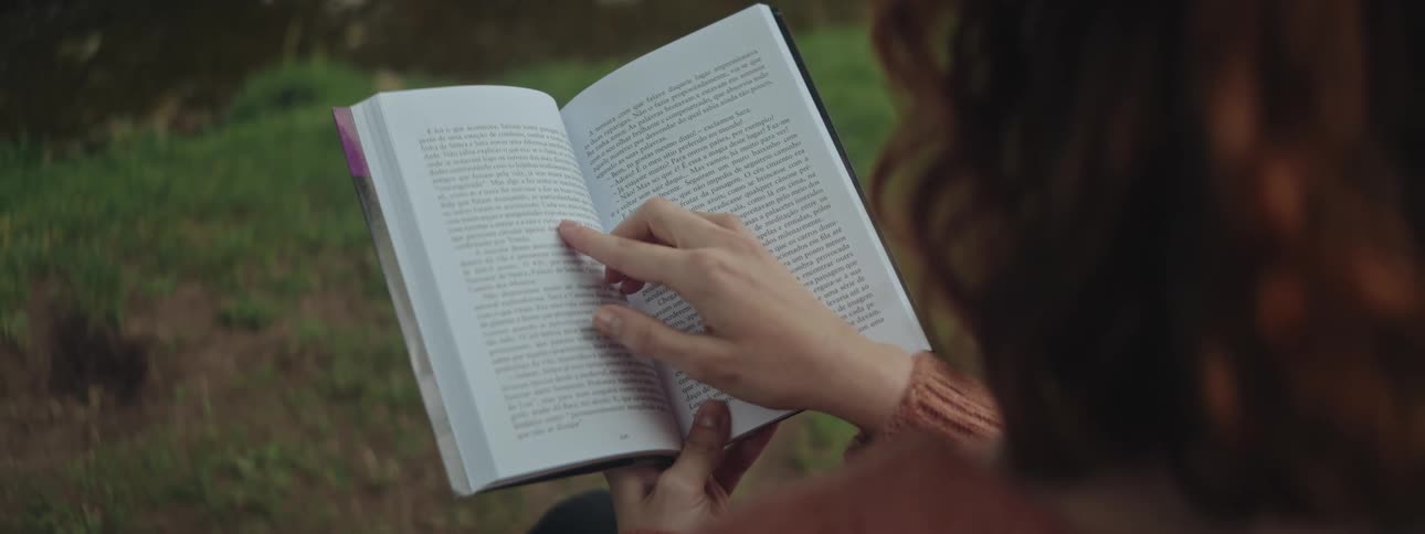 Woman reads a book outside in the grass on a sunny day