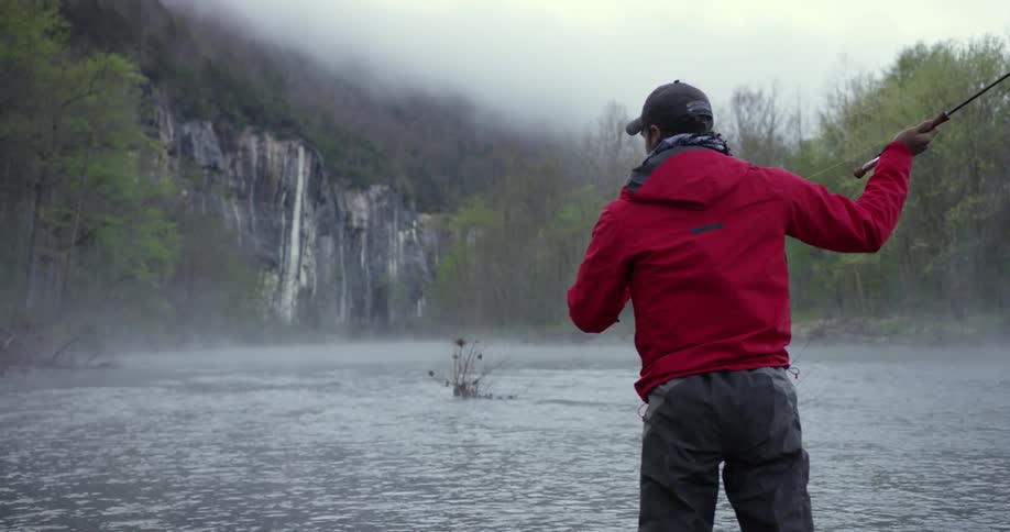 Bearded man fly fishing in a river on a very overcast day