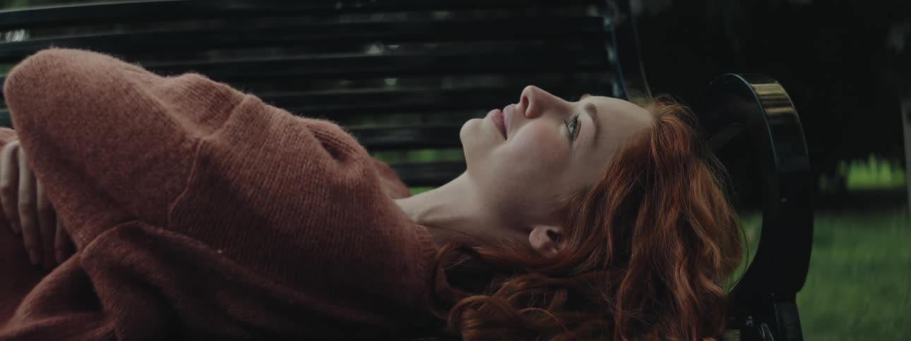 A clip of a lady laying on a bench and smiling