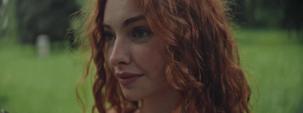 Redheaded woman smiles while outdoors in a field