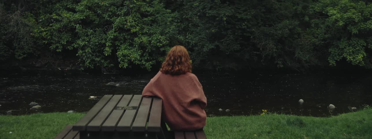 A woman sits at a bench watching a stream