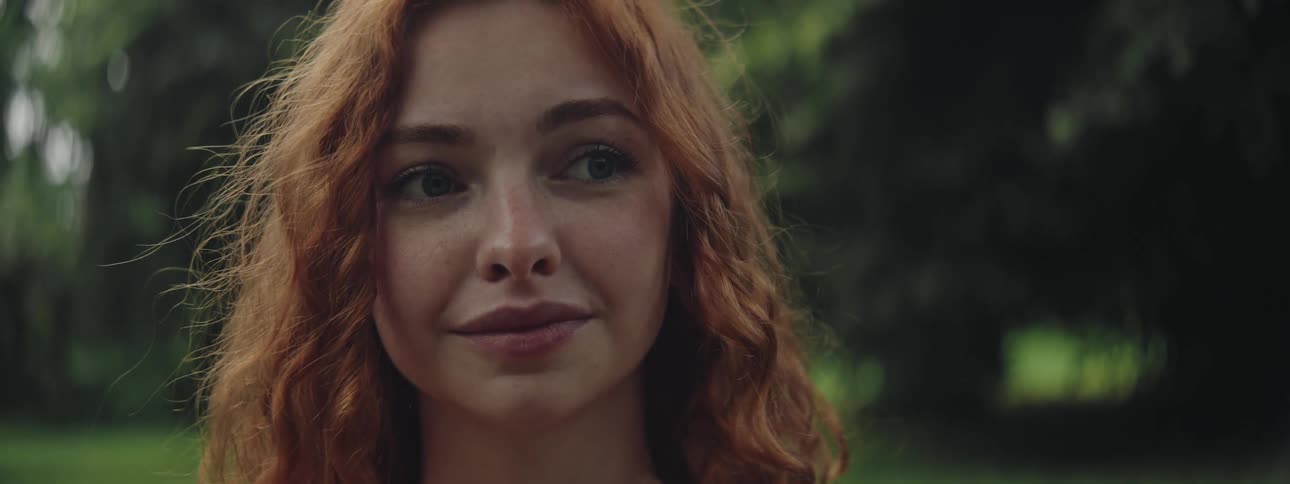 A woman with wavy red hair looks away in a green field