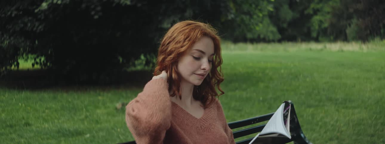 Young woman sitting on a bench in a space of grass and trees reading a book