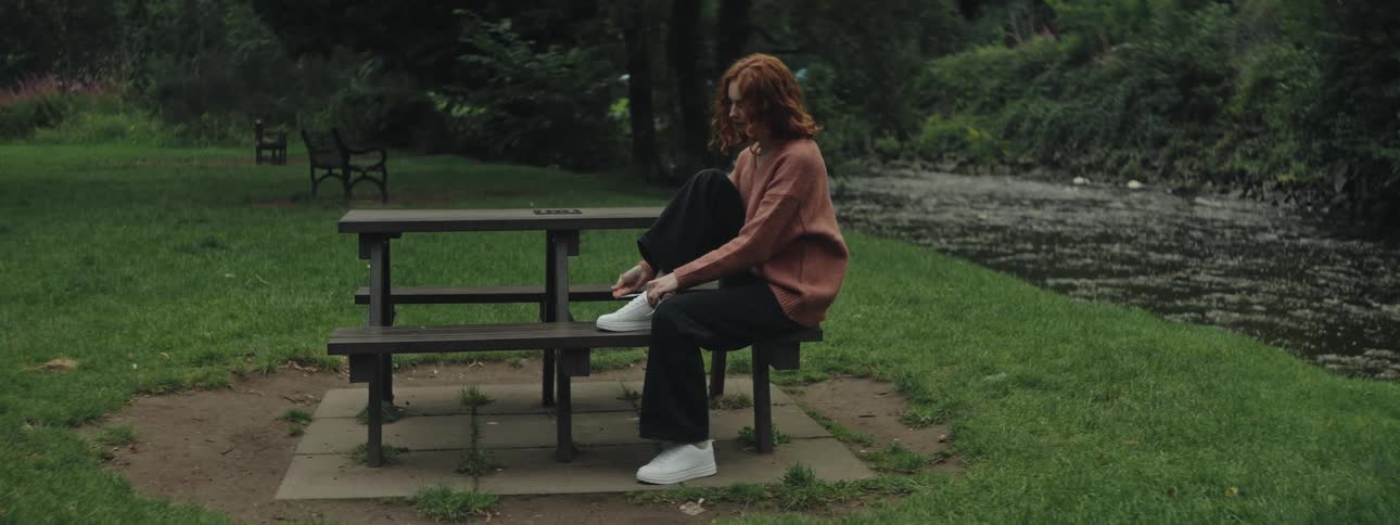A woman is tying her shoes by the stream