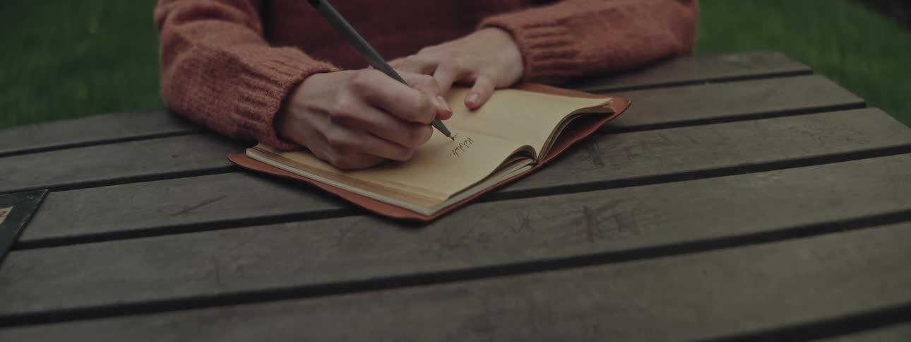 Hands of a woman writing in a notebook on top of a wooden table
