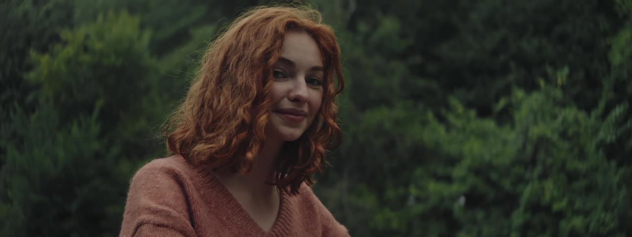 Redhead woman in a natural setting with trees in the background smiling