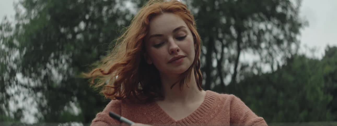 Woman with red hair and a brown sweater writes down in a notebook