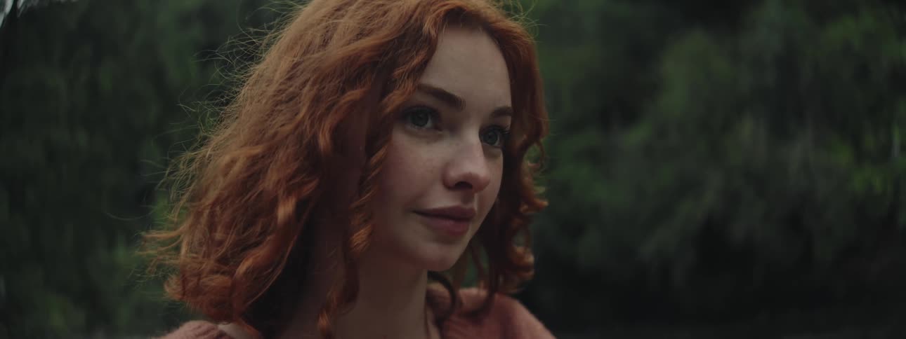 Portrait of a young redhaired woman in an outdoor space with trees in the background