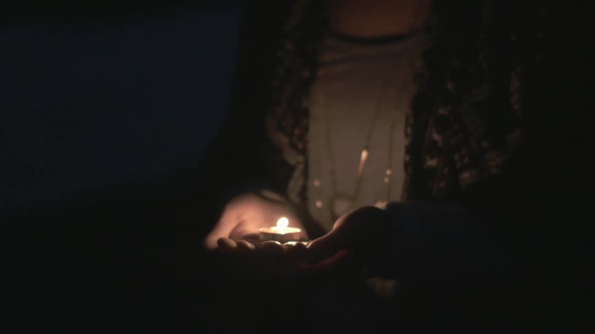 Person holding a small candle in a dark area