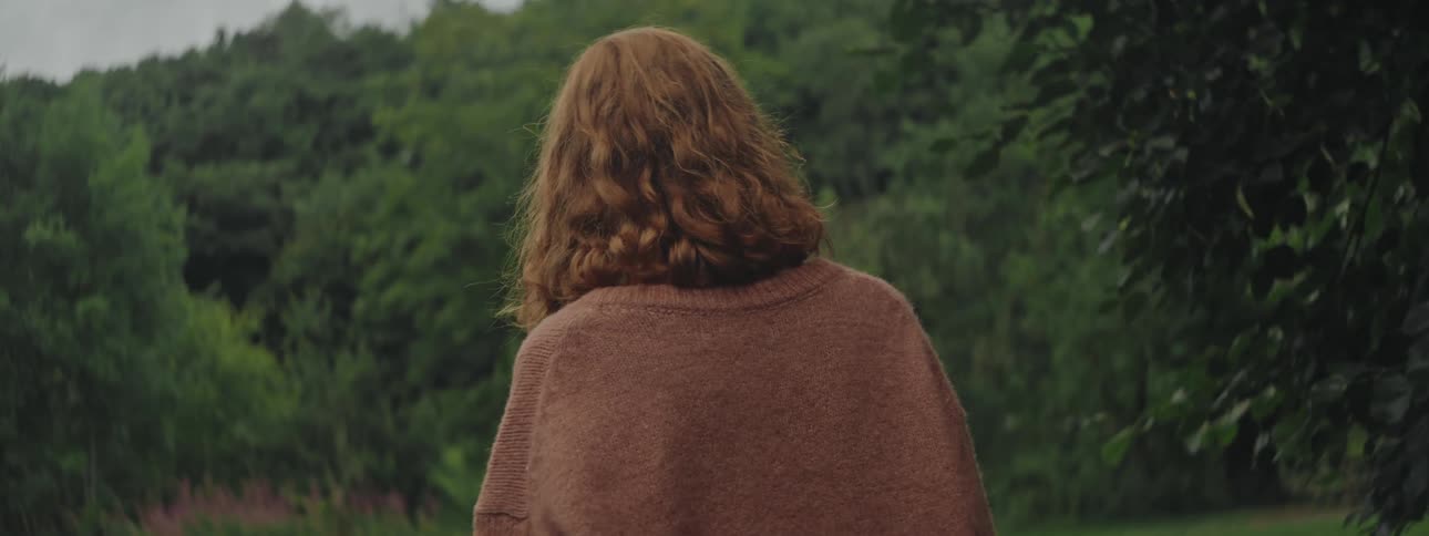 Red haired woman walks through a clearing in the woods