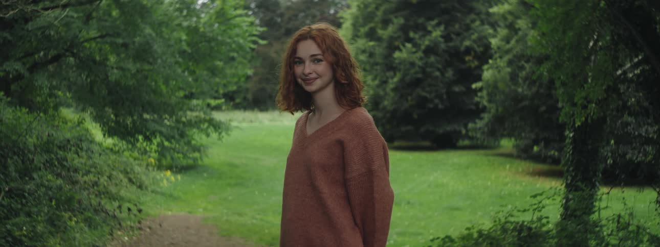 Redhead woman smiling in an area with grass and trees