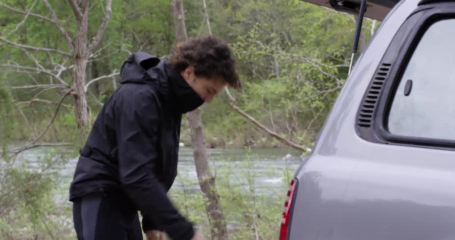 A man pulls his pants up and puts a beach towel in the trunk