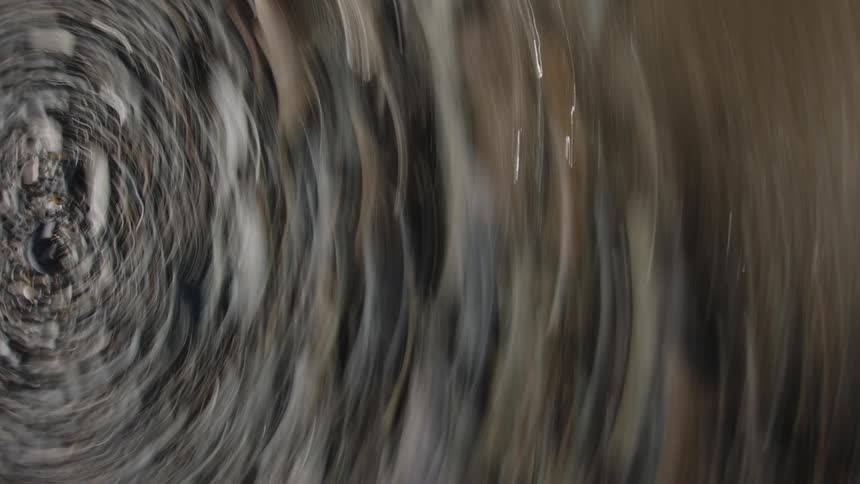 A blurred image of smooth rounded stones partially submerged in water next to the ocean