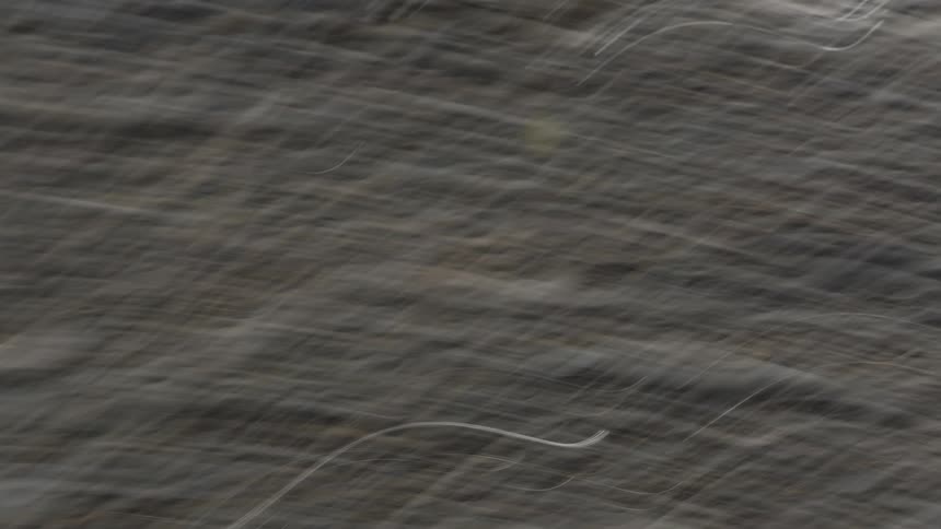 A blurred image of smooth rounded stones partially submerged in water next to the ocean