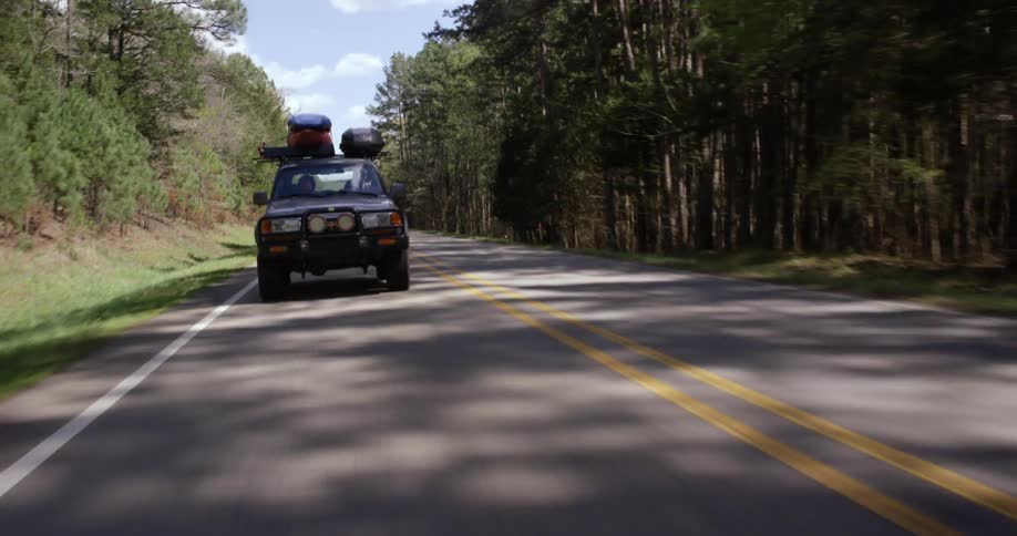 A person driving a truck with equipment on top down a country road