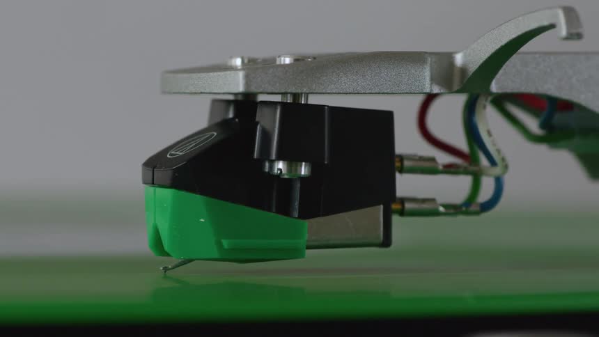 A closeup of a green cartridge on a turntable with a needle resting on a vinyl record