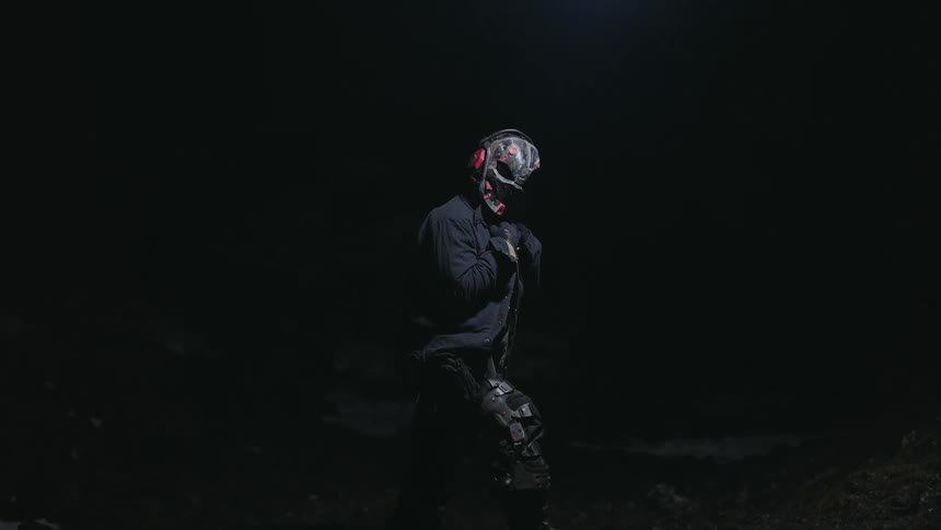 A masked figure wearing a dark tactical outfit with a weathered almost postapocalyptic look