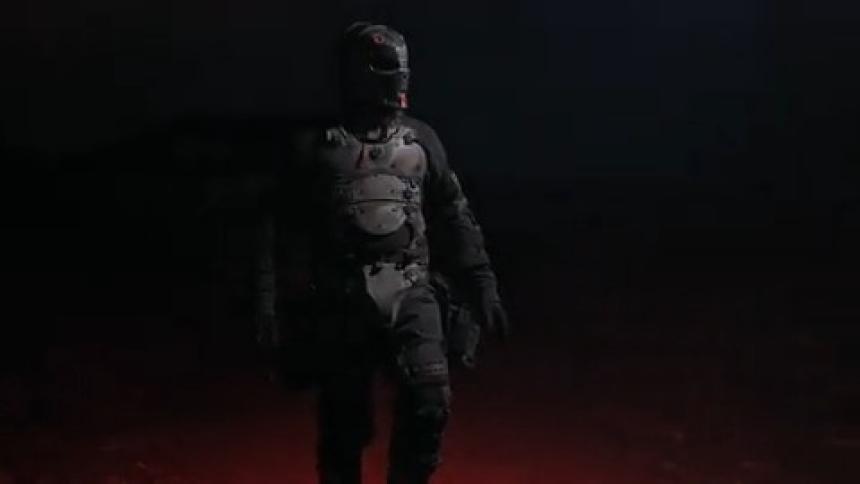 A man wearing armor and a mask walk at night